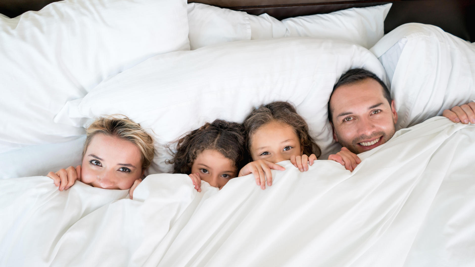 family hiding under sheets in bed